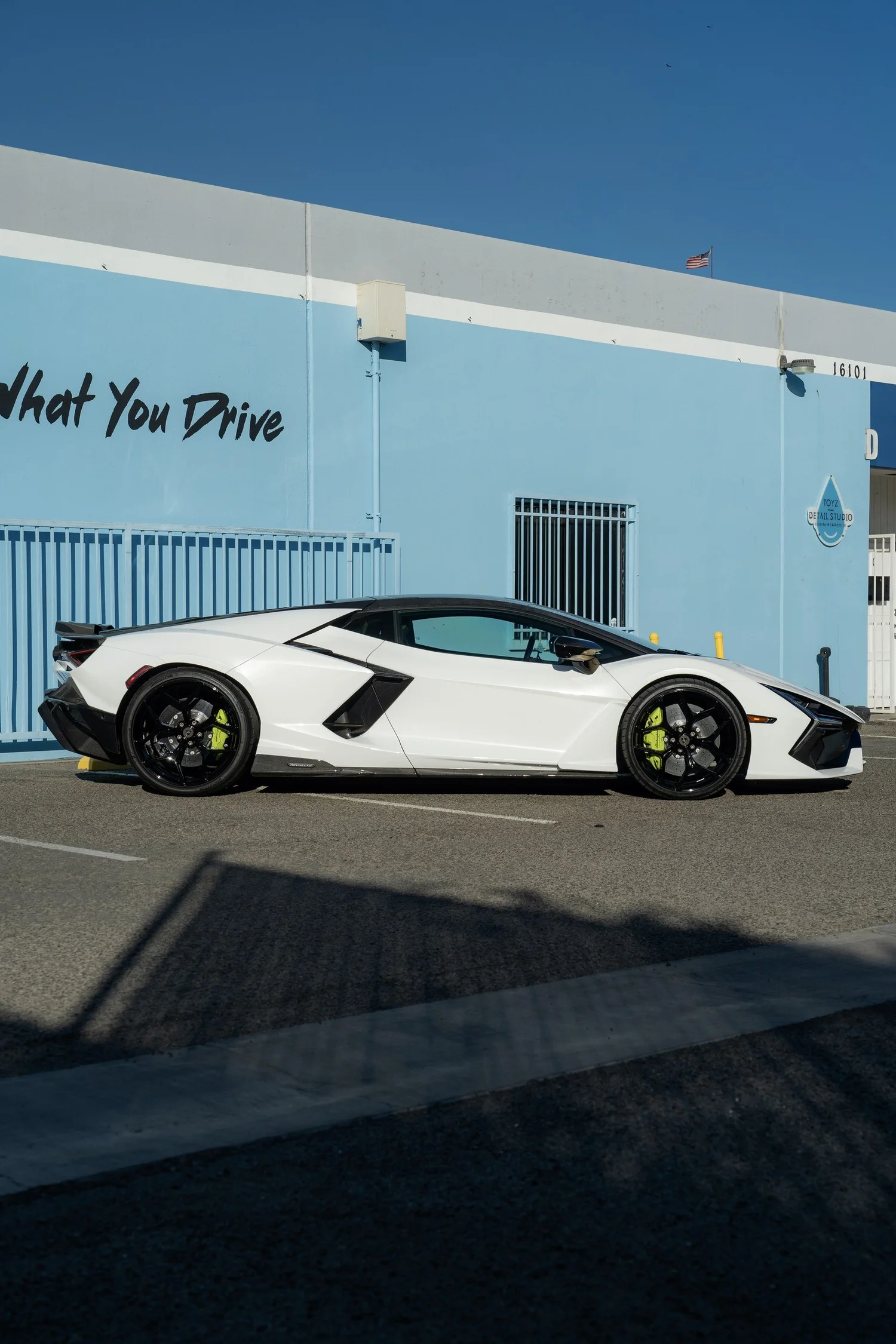 Full side profile of the white Lamborghini Revuelto with black wheels outside the studio.