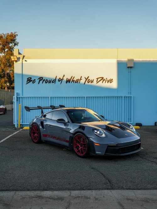Grey Porsche GT3 RS with red wheels, red side graphics and a rear wing in front of the Toyz studio wall