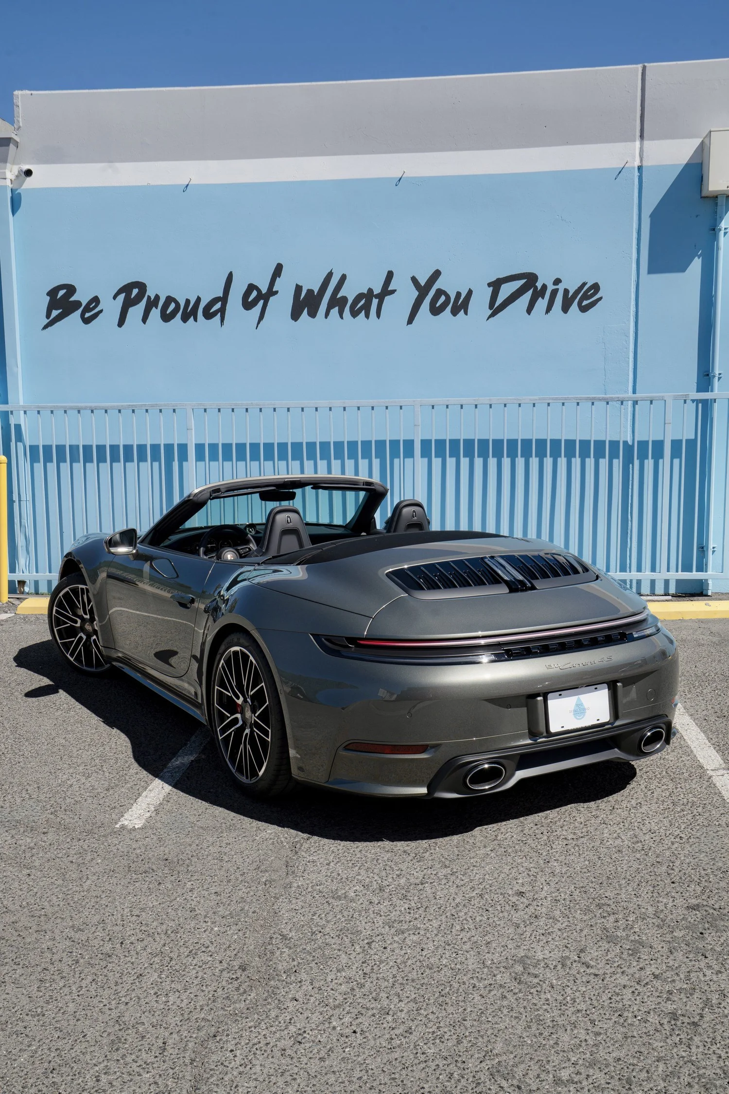 Complete rear three-quarter view of the Vanadium Grey Porsche 911 Carrera 4S Cabriolet with its roof lowered outside Toyz Detail Studio.