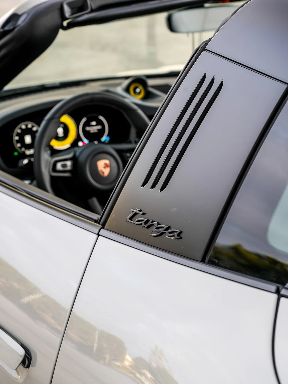 Black Porsche Targa roof bar with vent slots and targa lettering beside the open cabin