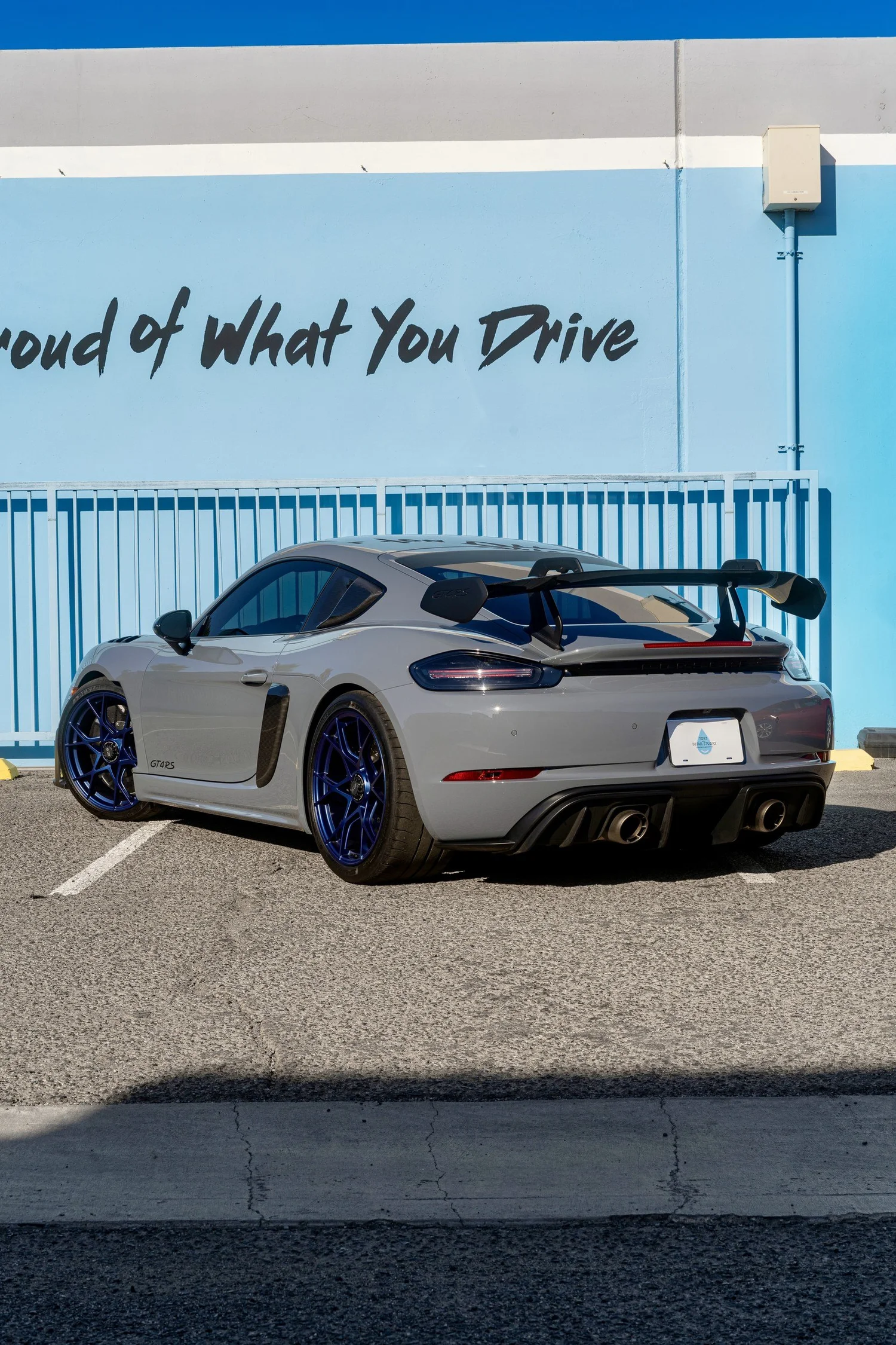 Low rear three-quarter view of the Arctic Grey GT4 RS with blue wheels, carbon rear wing and rear diffuser outside Toyz.