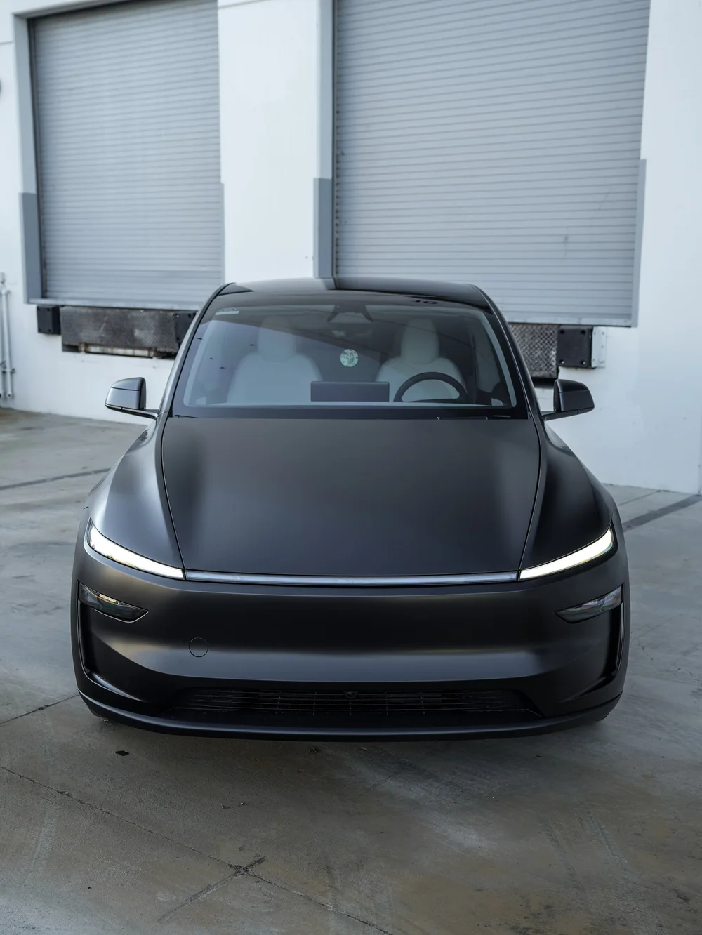 Tesla Model Y with 3M Satin Black vinyl, direct front whole-car view with the horizontal light strip