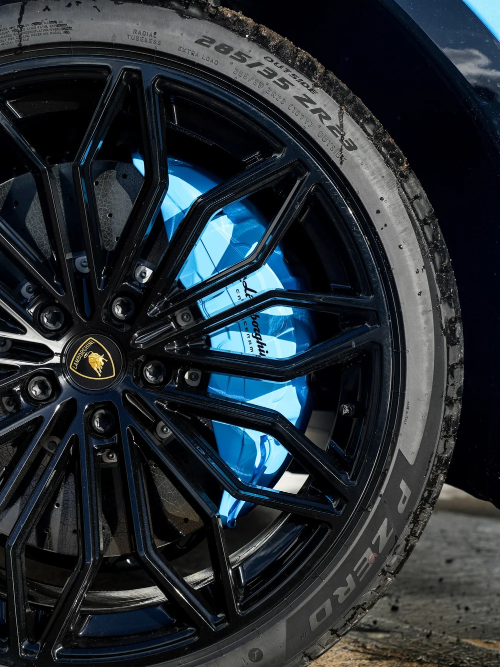 Close view through the Urus SE black wheel spokes to the light-blue brake caliper and Lamborghini center emblem