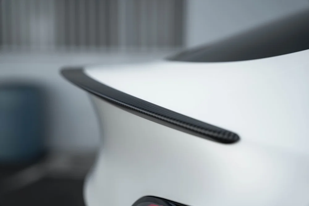 Close side view of the Tesla Model Y rear spoiler edge above the Satin Pearl White hatch