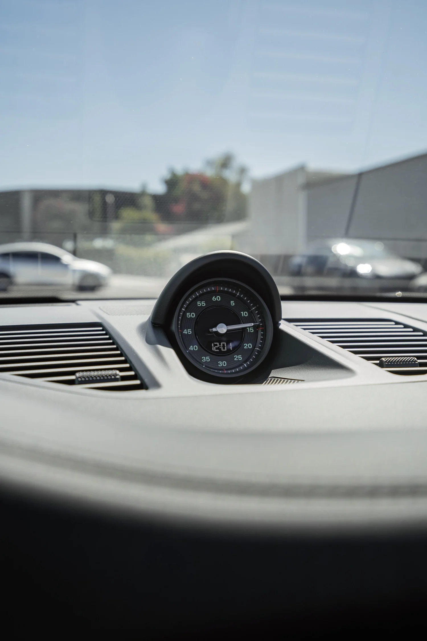 Dashboard clock in the Porsche 911 Cabriolet, with the windshield and parking area softly blurred behind.