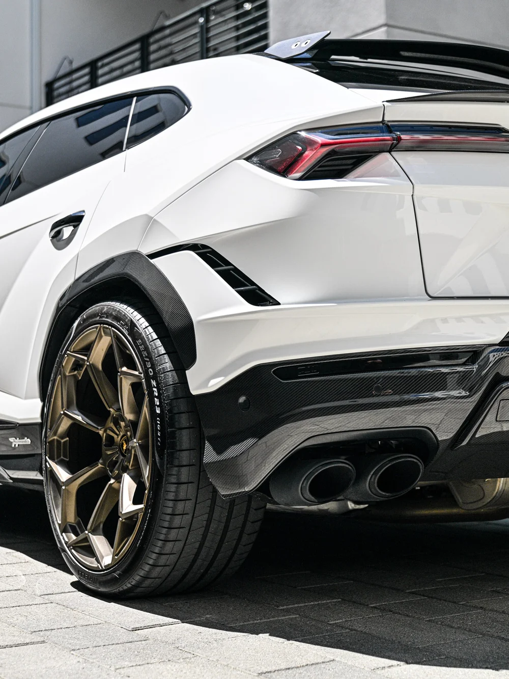 Close Urus rear corner showing a bronze-toned wheel, pale blue caliper and paired exhaust outlets