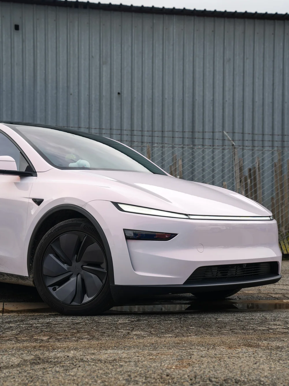Close front-quarter view of the Pale Blush Pink Tesla Model Y showing the front wheel, hood and light bar