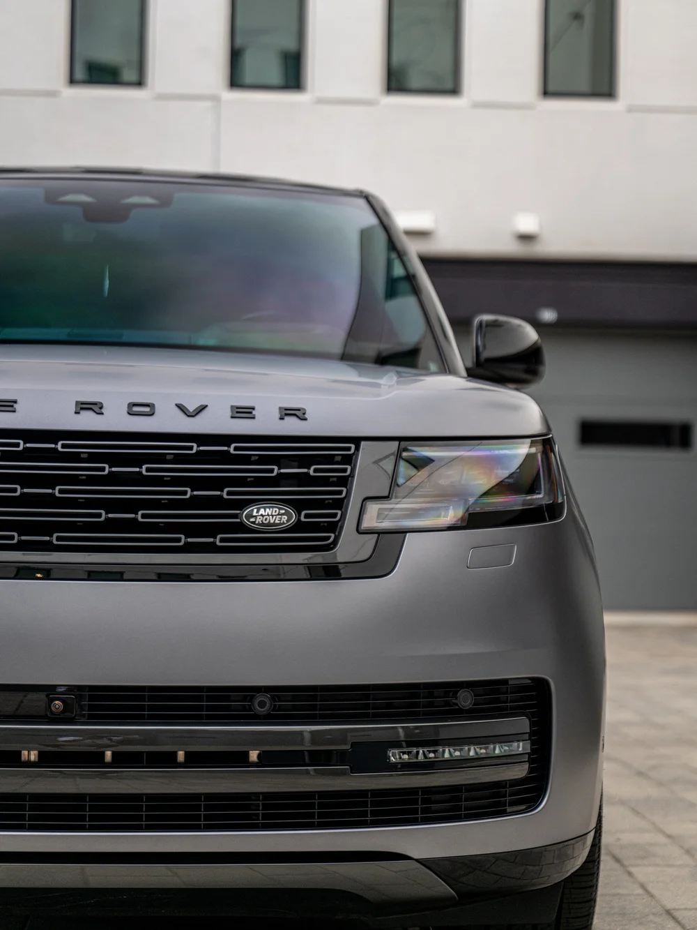 Range Rover grille and headlight close-up beside the satin front bumper, with the gloss black mirror visible behind.
