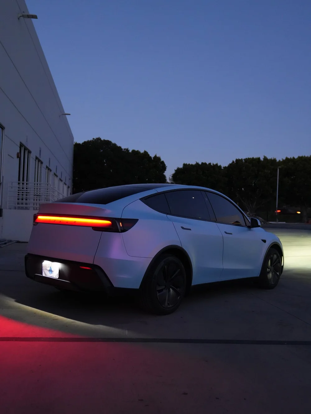 Rear three-quarter view of a Tesla Model Y with white-to-blue vinyl under the evening sky