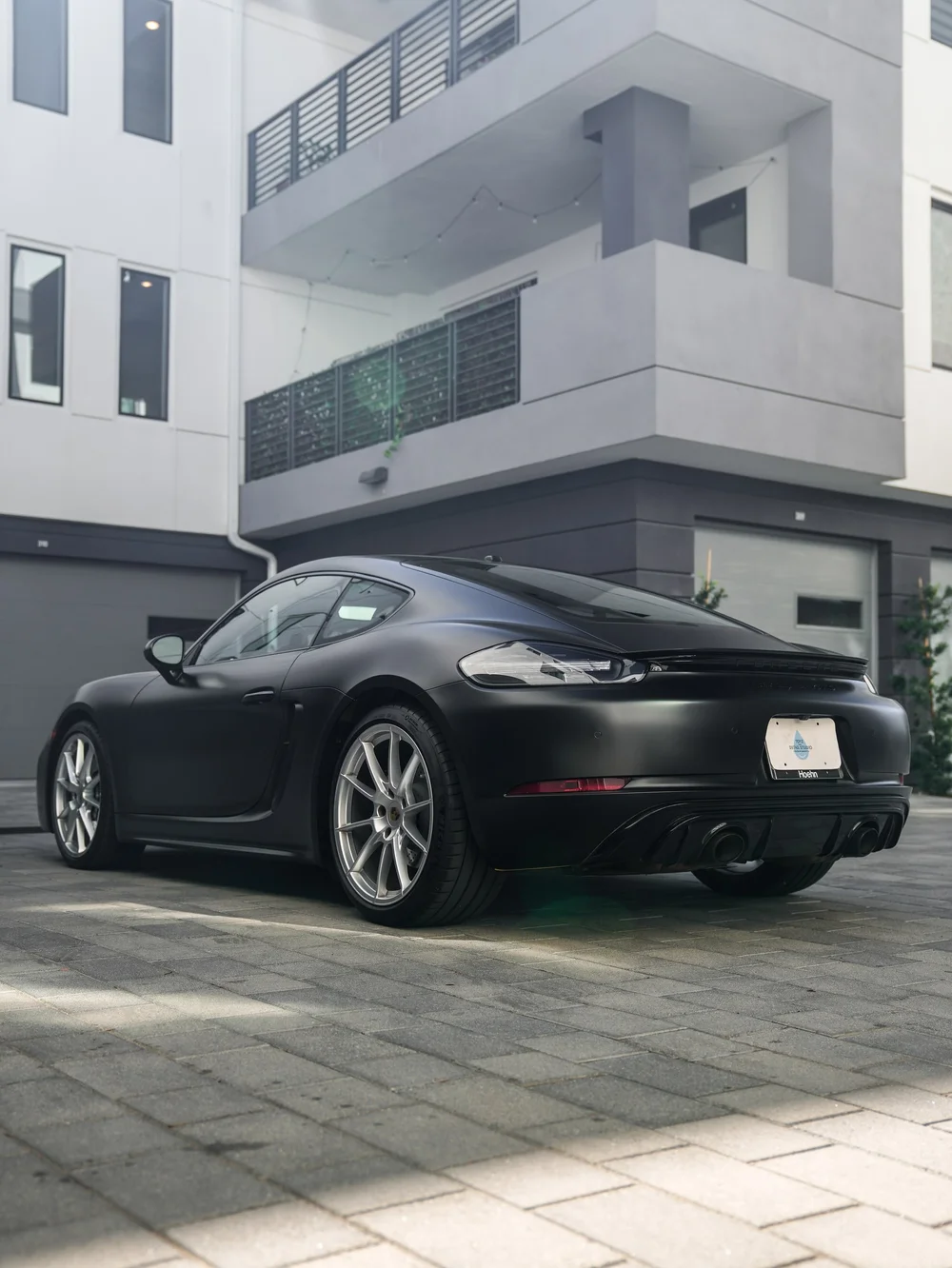 Low rear three-quarter view of the Porsche 718 Cayman GTS with 3M Satin Black vinyl wrap