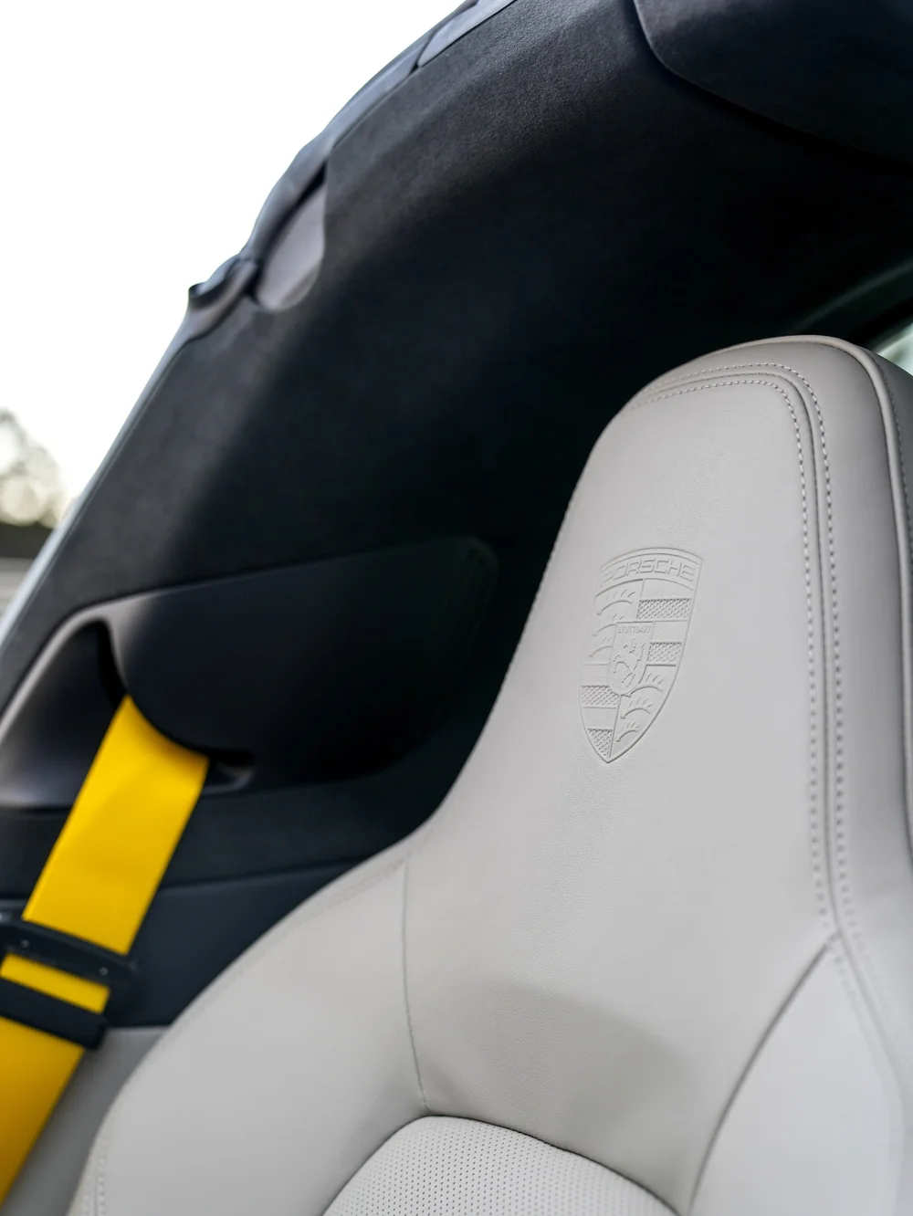 Light Porsche front seat with an embossed crest and yellow seat belt