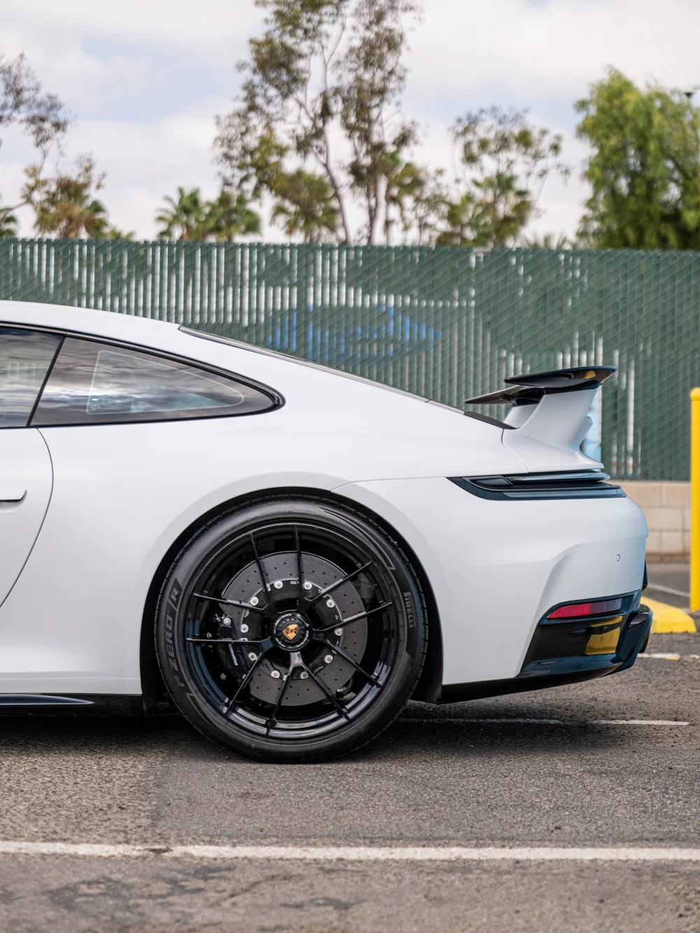 Rear quarter of a Porsche 911 Carrera 4 GTS showing the rear wing, center-lock rear wheel and satin-white body finish