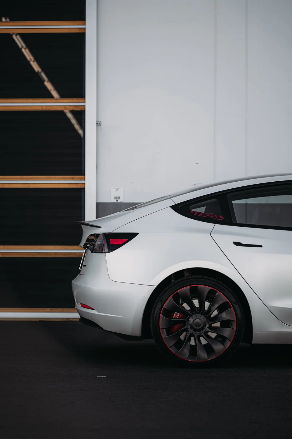 Rear-quarter and rear-wheel view of the Satin Pearl White Tesla Model 3 with red wheel-rim accents visible