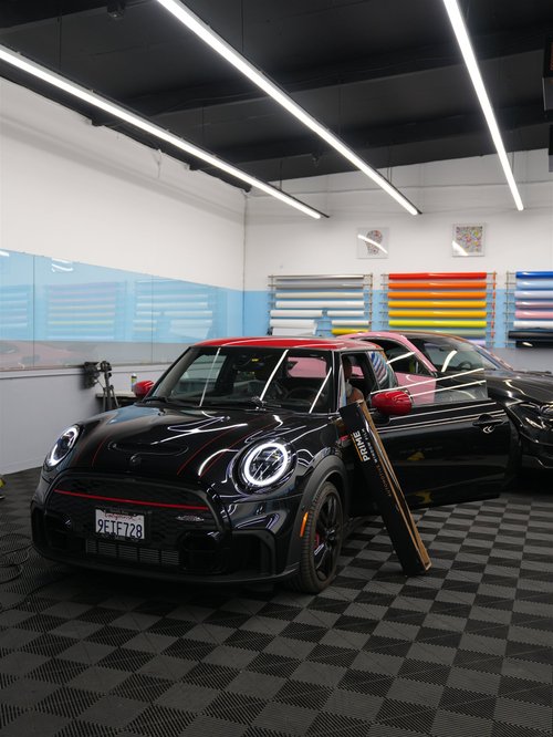 Black MINI Cooper with a red roof and XPEL PRIME window-film packaging inside Toyz Detail Studio.
