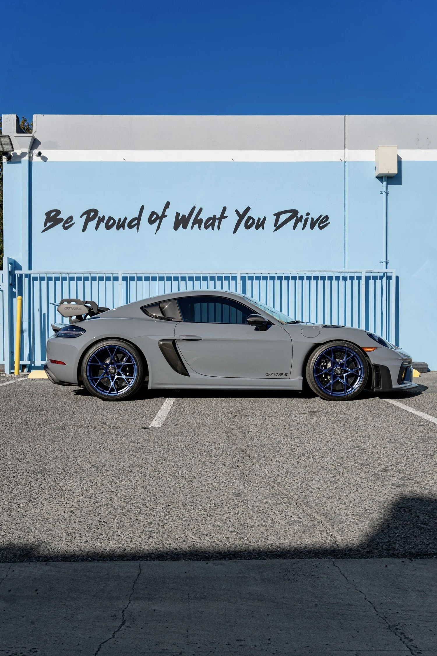 Complete side profile of the Arctic Grey GT4 RS with blue wheels, side intake and rear wing against the Toyz wall.