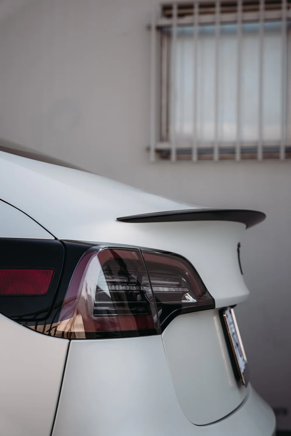 Rear trunk, taillight and dark spoiler detail on the Tesla Model 3 with Satin Pearl White vinyl
