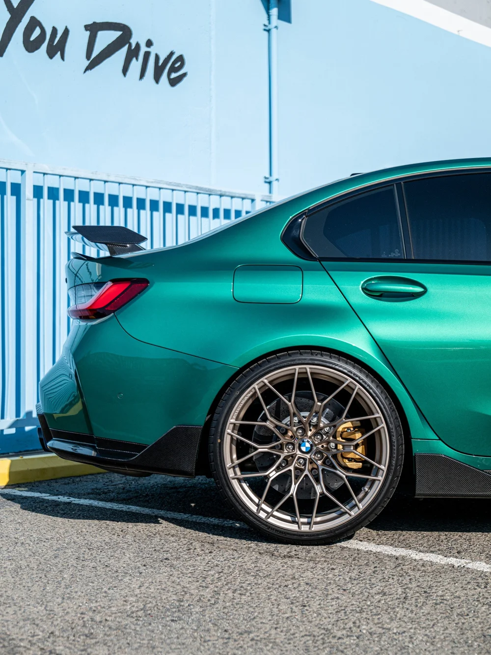 Rear wheel and quarter panel of the green BMW M3 with the raised M Performance rear wing