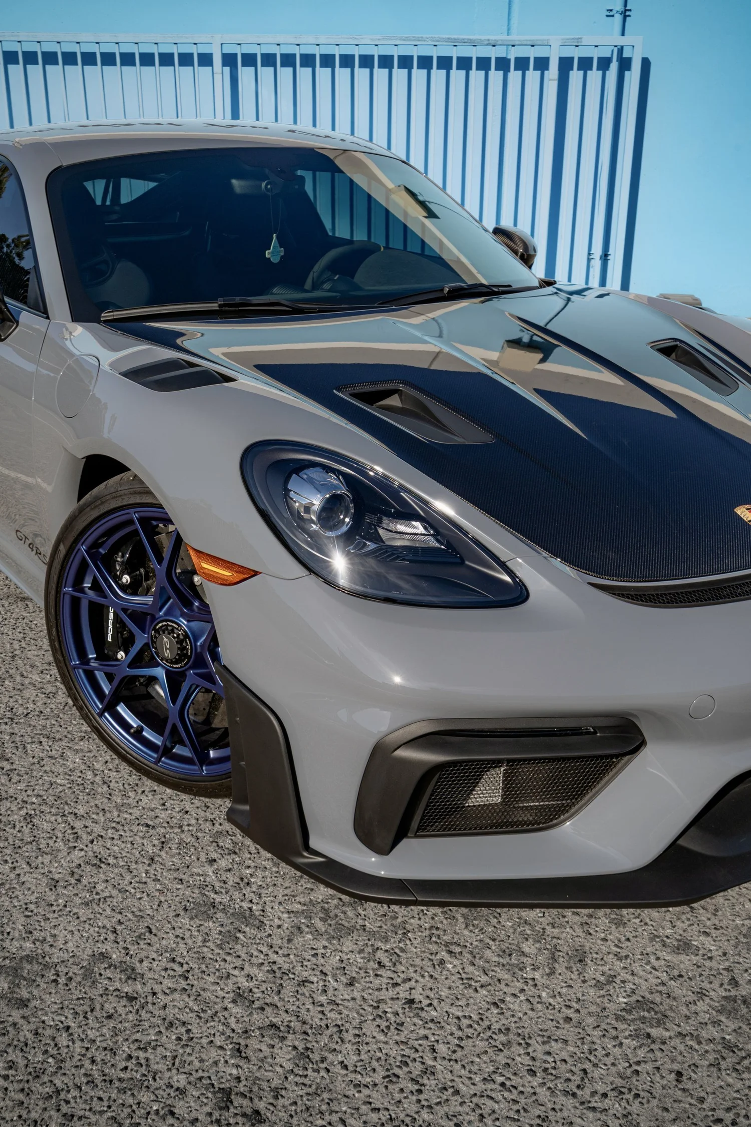 GT4 RS front-quarter close-up showing a blue wheel face, headlight, exposed carbon hood and Arctic Grey bumper.