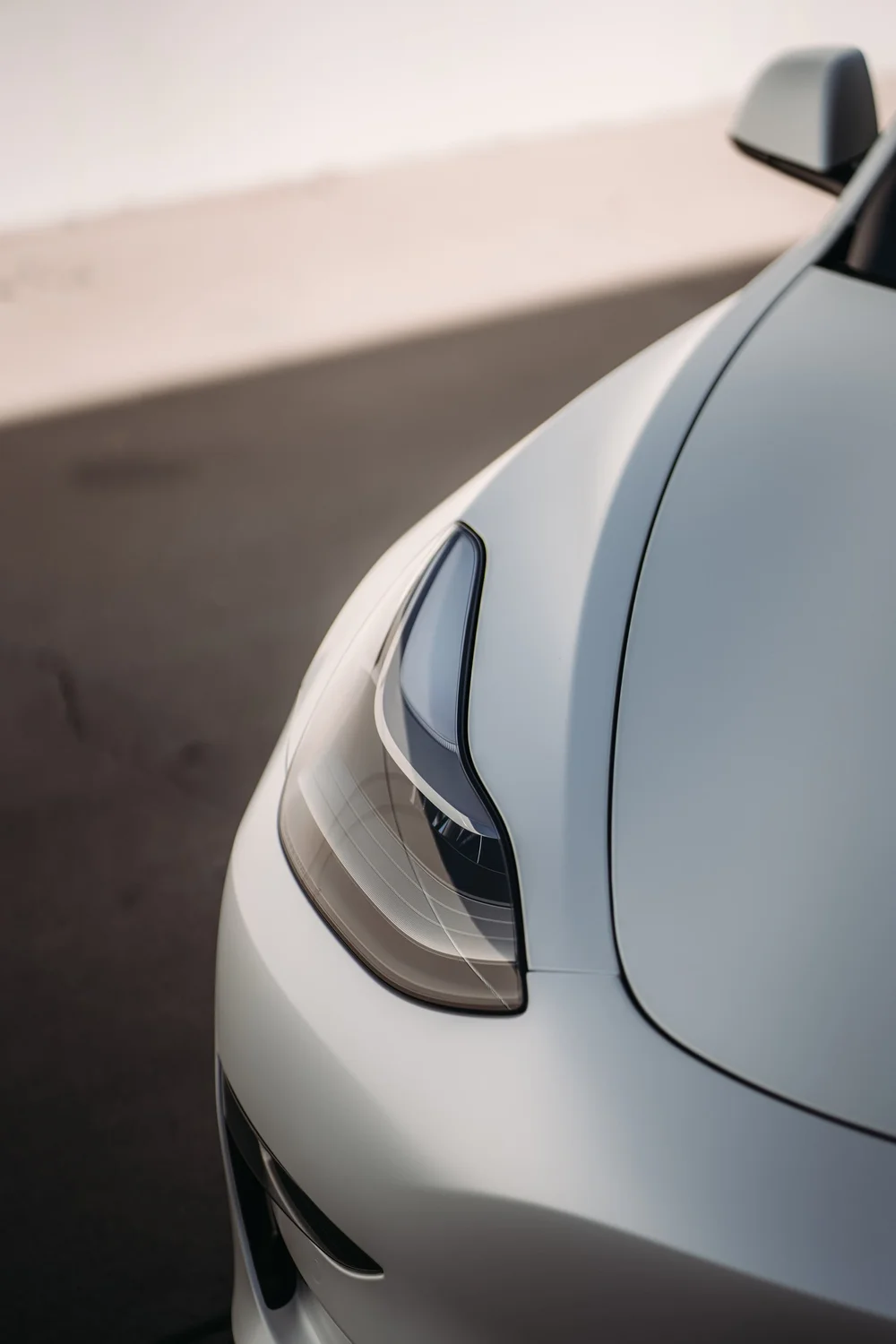 Front-headlight and hood-corner detail of the Tesla Model 3 with 3M 2080 Satin Pearl White vinyl