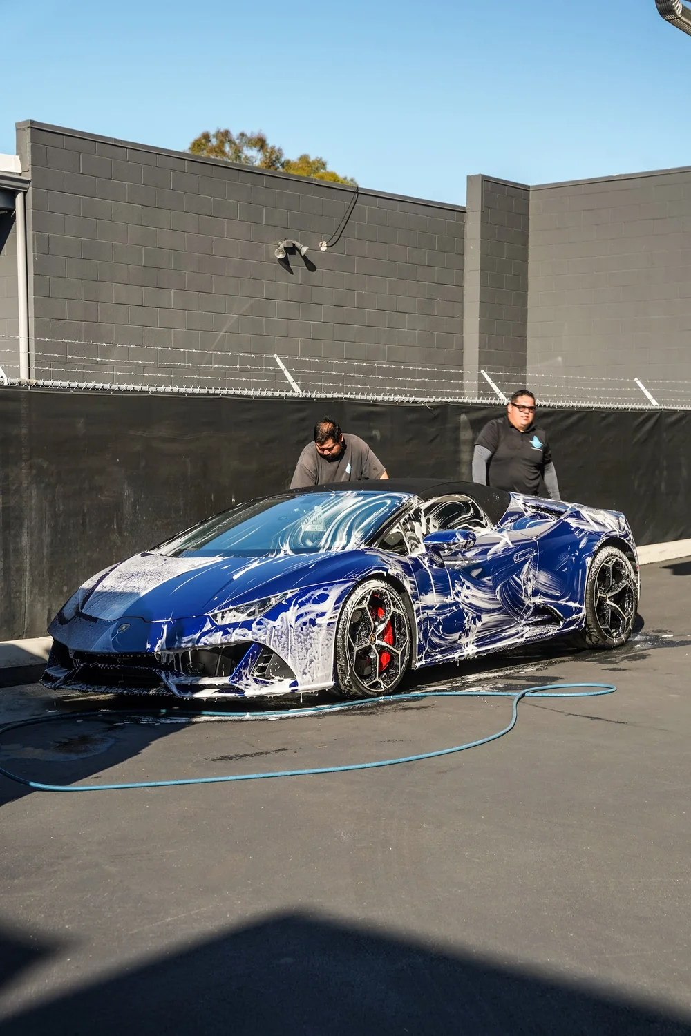 Blue Lamborghini covered in foam during washing with a technician beside it