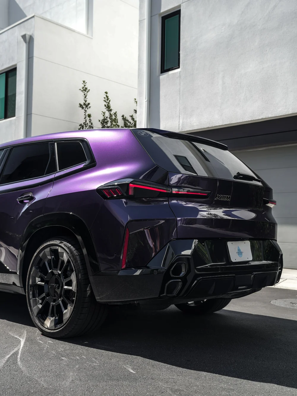 Low rear-quarter view of the BMW XM showing Venetian Mauve colored PPF and stacked exhaust outlets