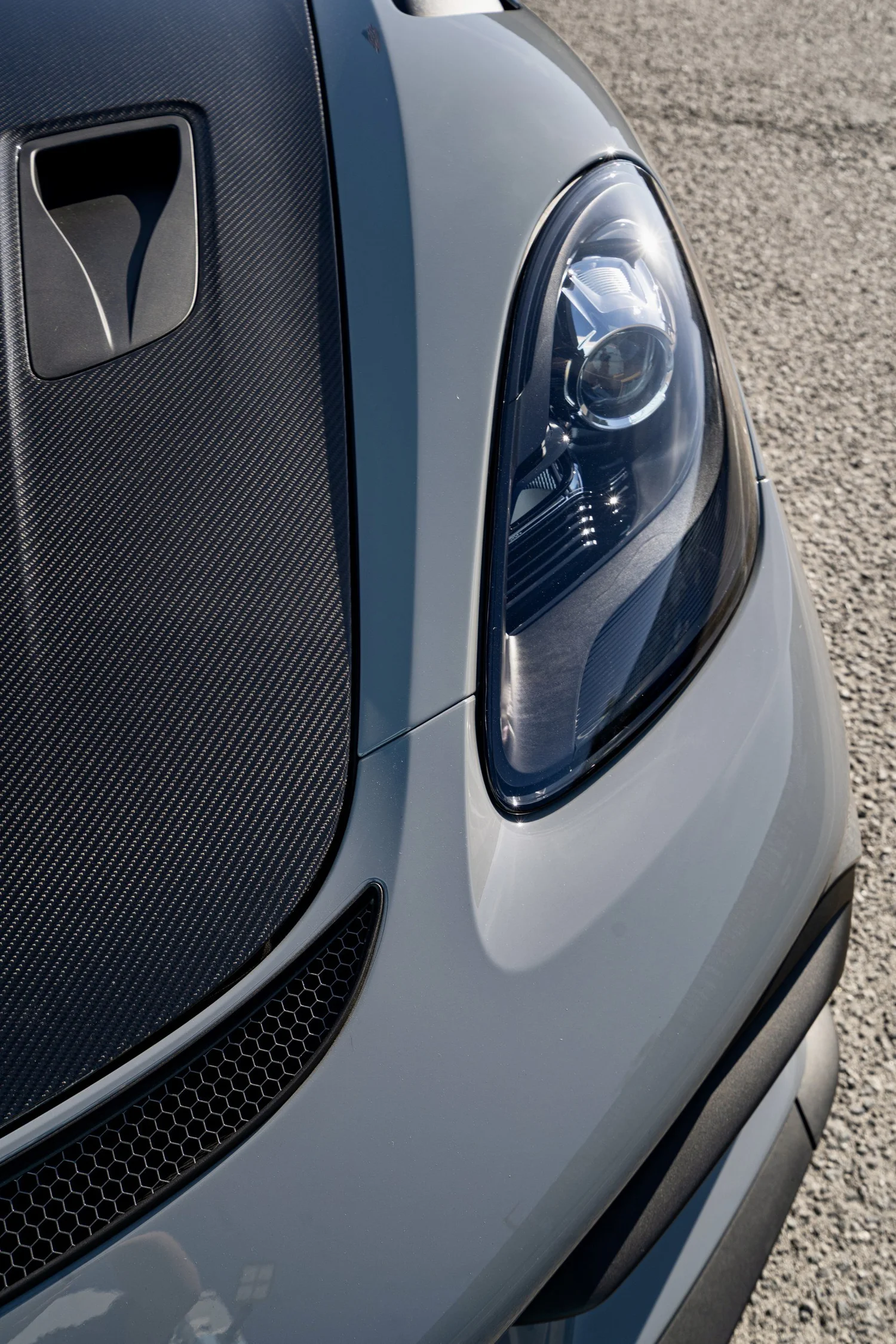 Close-up of a GT4 RS headlight next to the exposed carbon hood vent and Arctic Grey front bodywork.