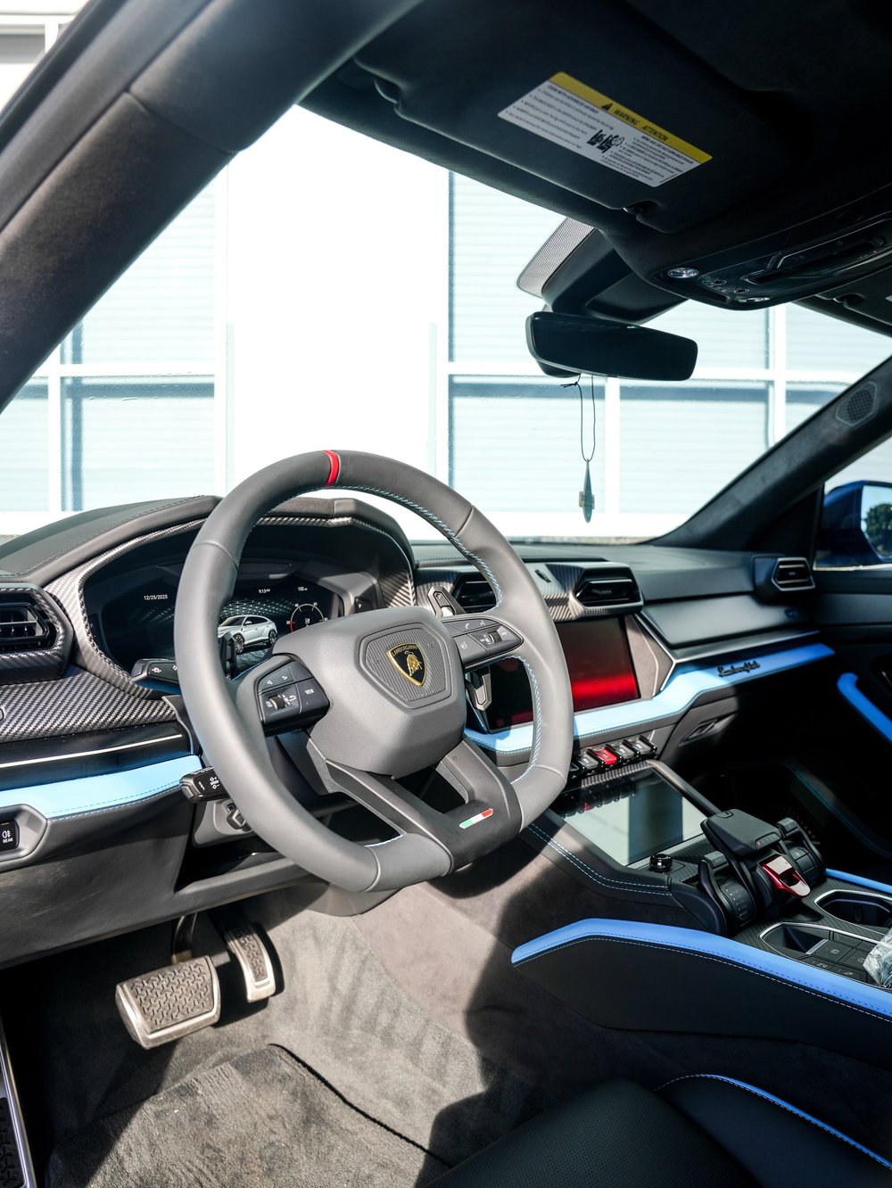 Urus SE cabin with Lamborghini steering-wheel emblem, instrument display, blue dashboard trim and center console