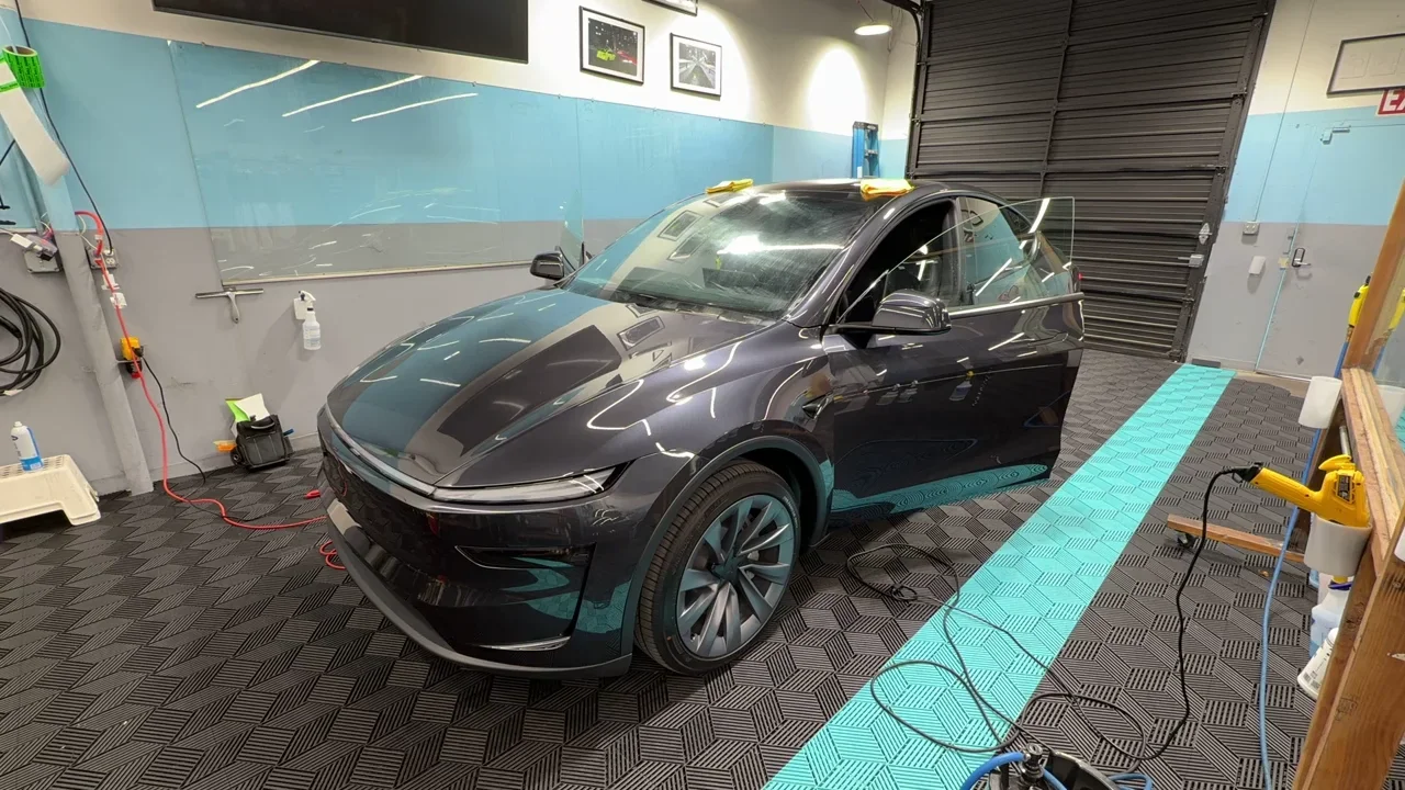 2027 Tesla Model Y — video frame showing the front and side with a door open inside the studio