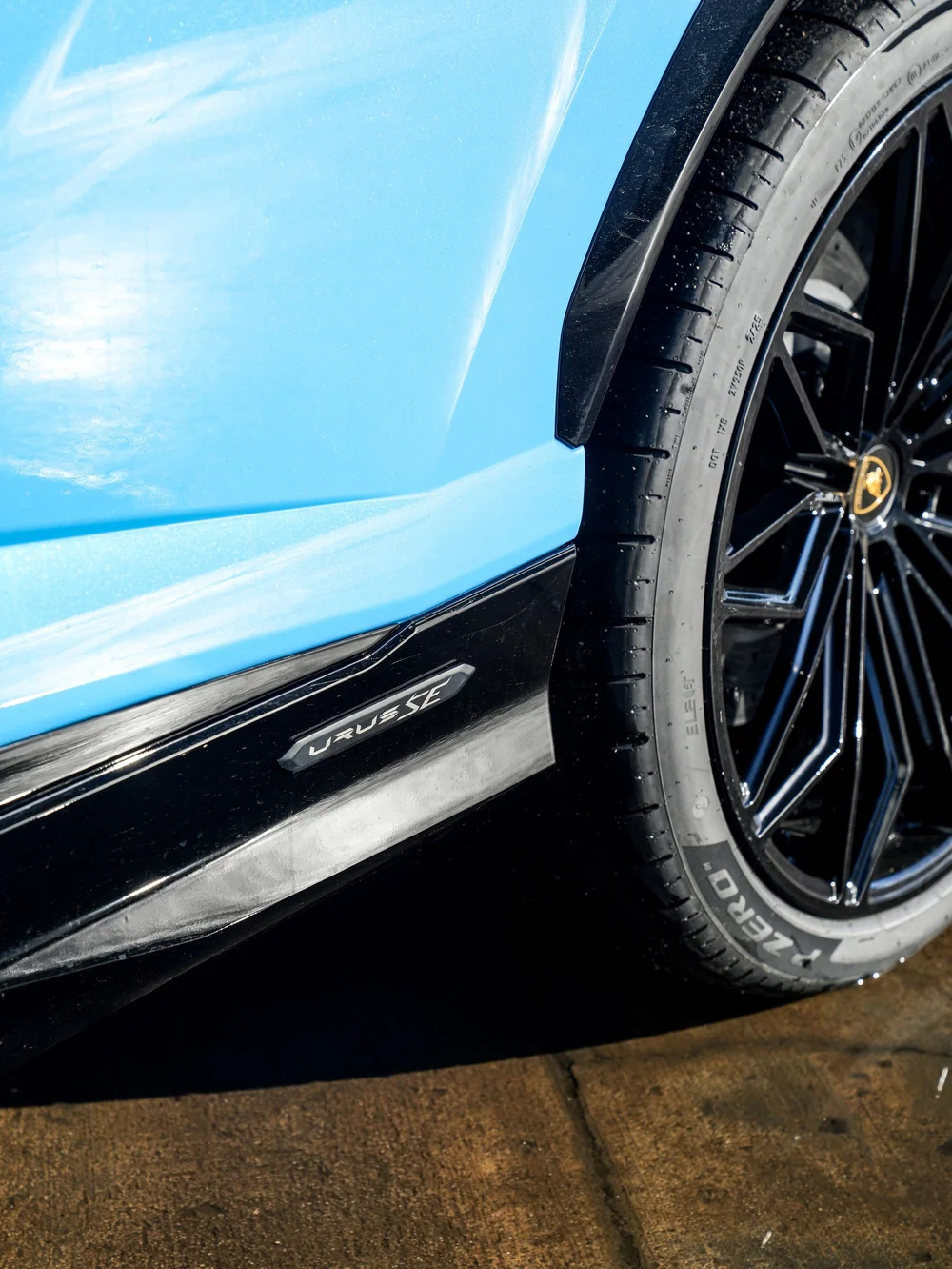 URUS SE lettering on the black lower side trim beside a wheel and light-blue body panel