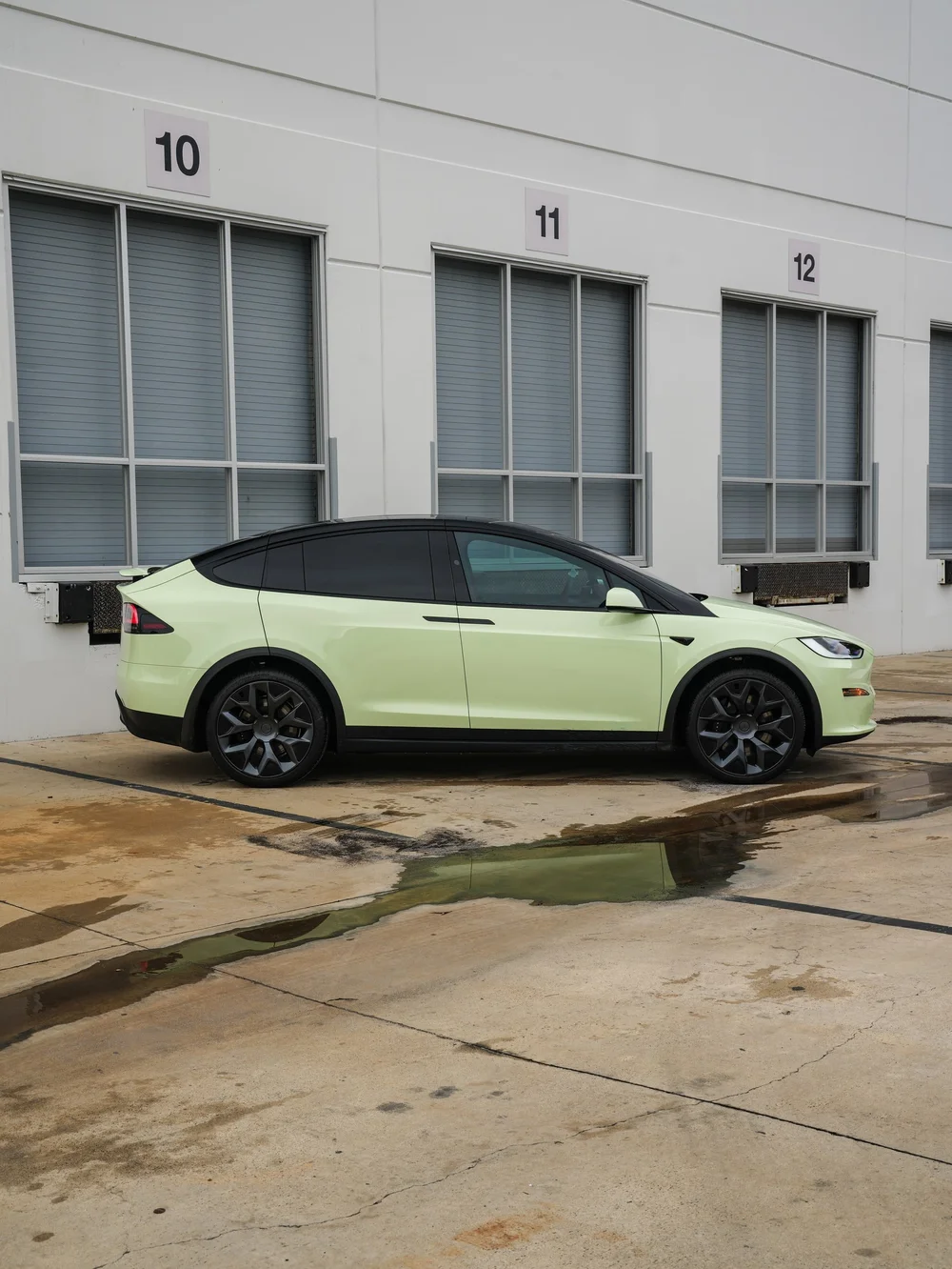 Full side profile beside the industrial building — Tesla Model X Avocado Green vinyl wrap project
