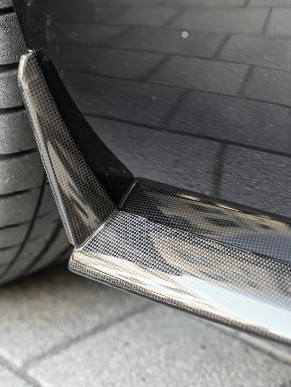 Dark patterned Ferrari lower trim beside the tire and paved ground