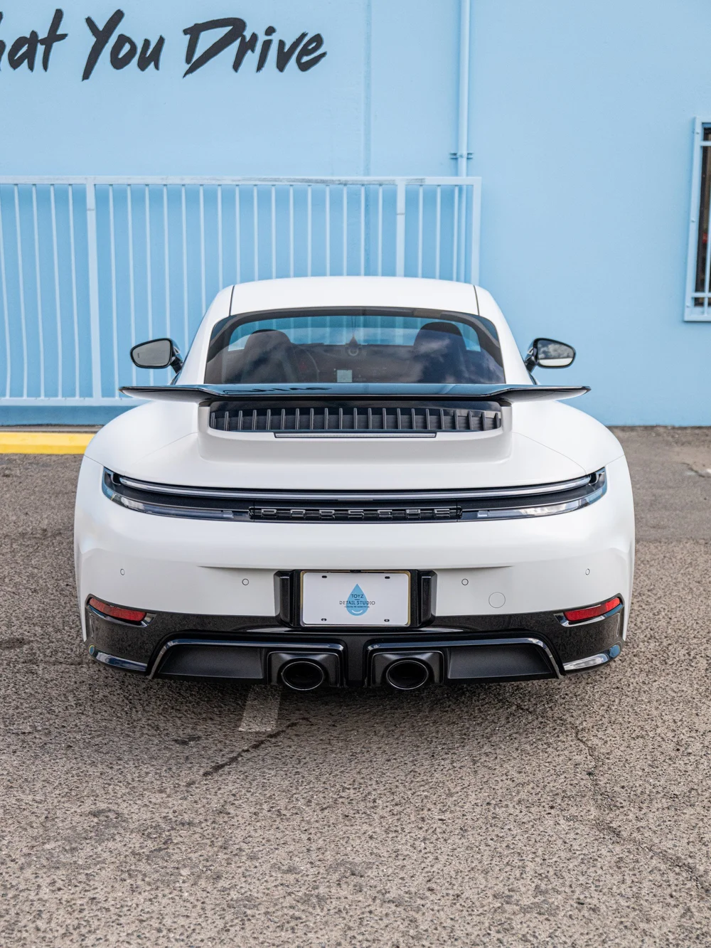 Straight rear view of a 2026 Porsche 911 Carrera 4 GTS showing the satin-white body, raised rear wing and gloss-black lower trim