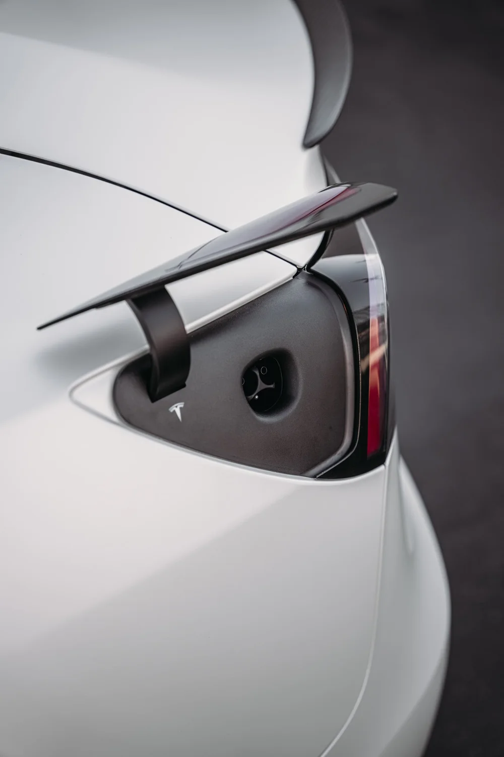 Open charge-port detail beside the rear light and Satin Pearl White bodywork of the Tesla Model 3