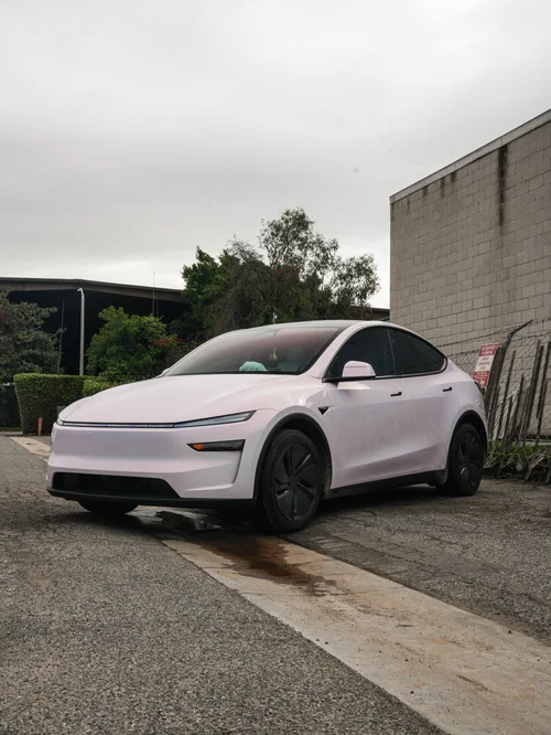 Opposite front three-quarter view of the Pale Blush Pink Tesla Model Y parked outside the studio