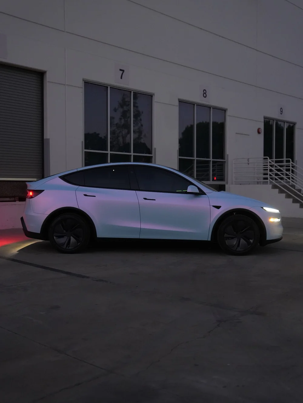 Full side profile of a Tesla Model Y with white-to-blue color-shifting vinyl outside the studio