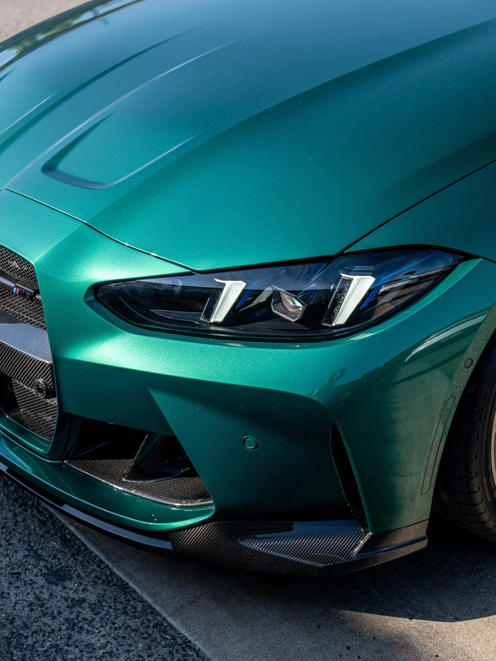 Close-up of the carbon front splitter and bumper aero beneath the green M3 headlight