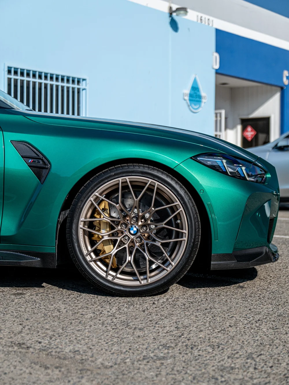 Front wheel and gold brake caliper beside the carbon side-skirt extension on the green M3