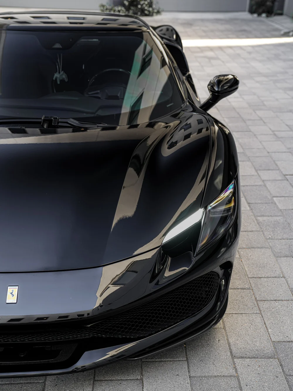 Elevated Ferrari front detail with one headlight, dark windshield and black bumper