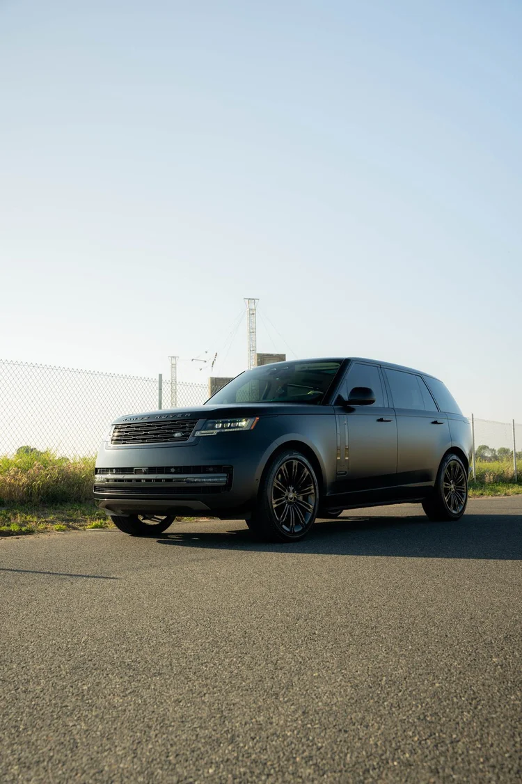 Matte-black Range Rover in a complete front three-quarter view facing left, with dark wheels beside a roadside fence.