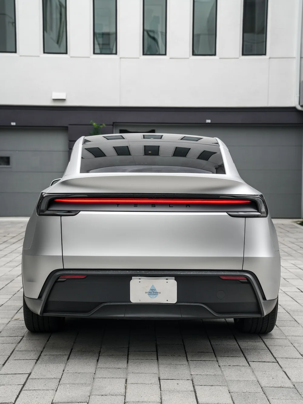 Complete rear view of the matte-silver Tesla Model Y with an illuminated red light bar
