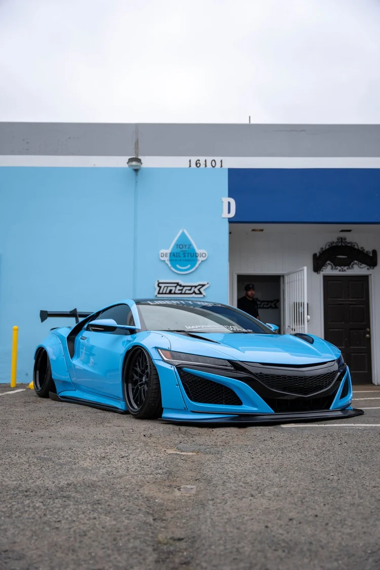 Bright blue sports coupe with a rear wing outside the Toyz studio entrance