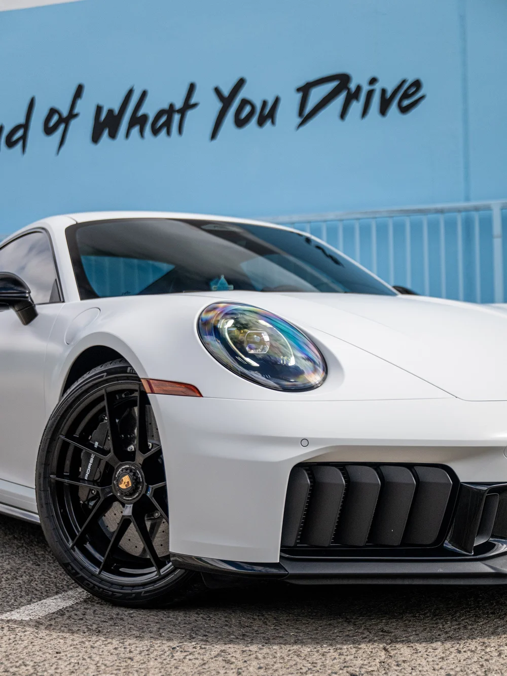 Front corner of a satin-white 2026 Porsche 911 Carrera 4 GTS, showing the headlight, center-lock wheel and gloss-black bumper trim