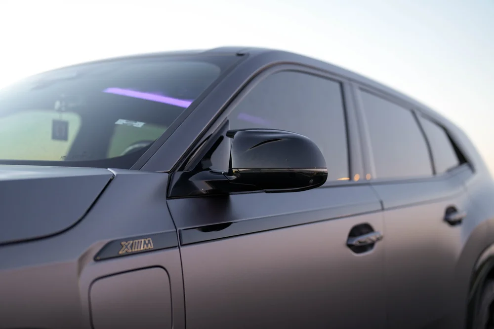 Wide side detail of the glossy black mirror, dark windows and matte-grey doors with their dark handles.