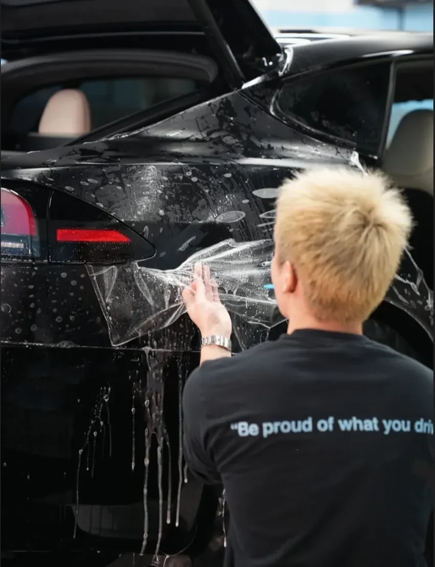 Max installing paint protection film on a black Tesla inside Toyz Detail Studio