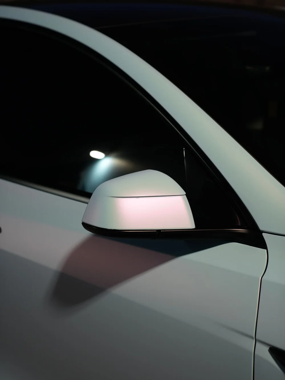 Mirror and front-door detail of a Tesla Model Y showing a pale color-shifting vinyl finish