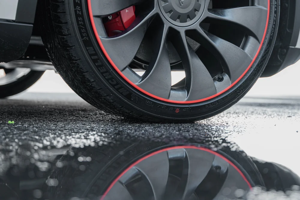 Tesla Model Y wheel and rim edging reflected in a puddle on the pavement