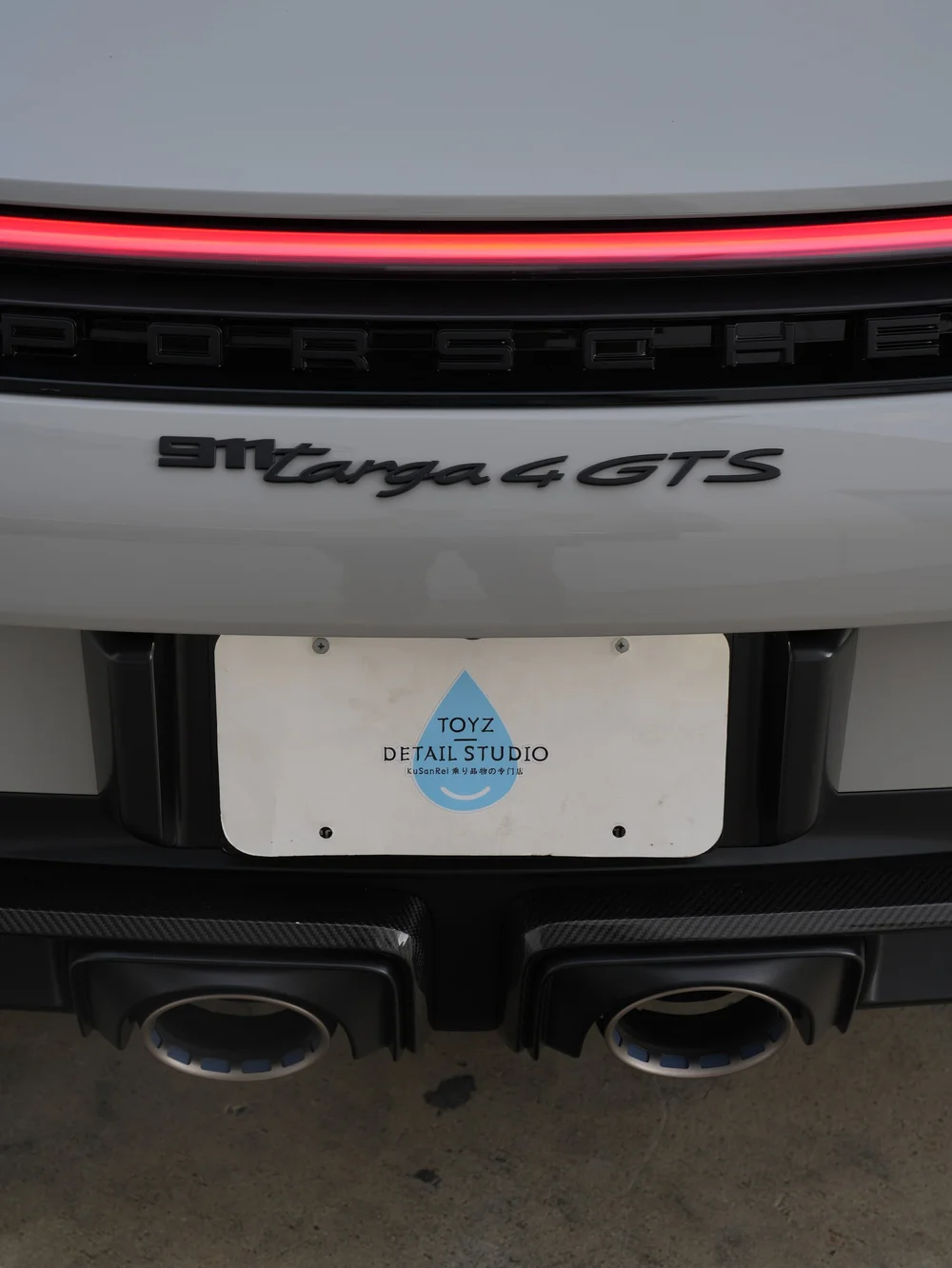 Close rear view of Porsche Targa badging, red light bar and two exhaust outlets