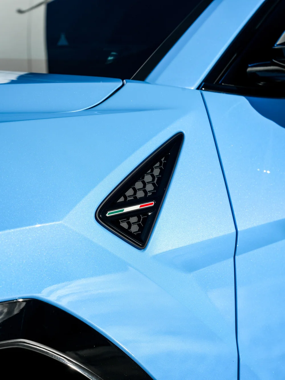Urus SE front-fender vent with a small Italian flag detail beside the light-blue door panel