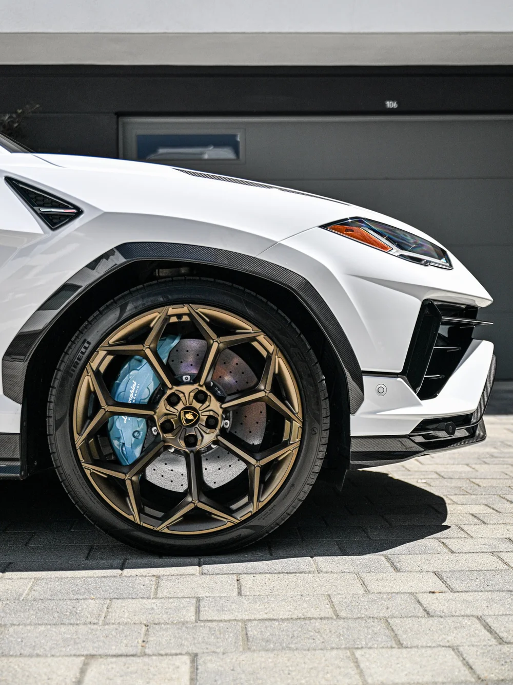 Bronze-toned Urus front wheel and pale blue brake caliper beneath the white fender