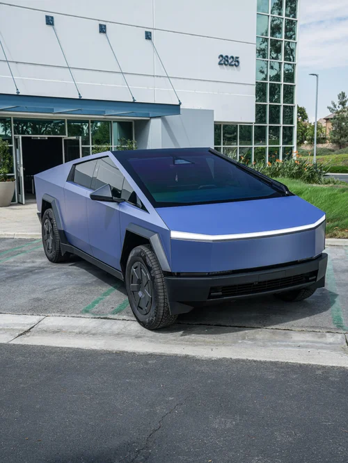 Matte blue Tesla Cybertruck viewed from the front and side beside a commercial building.